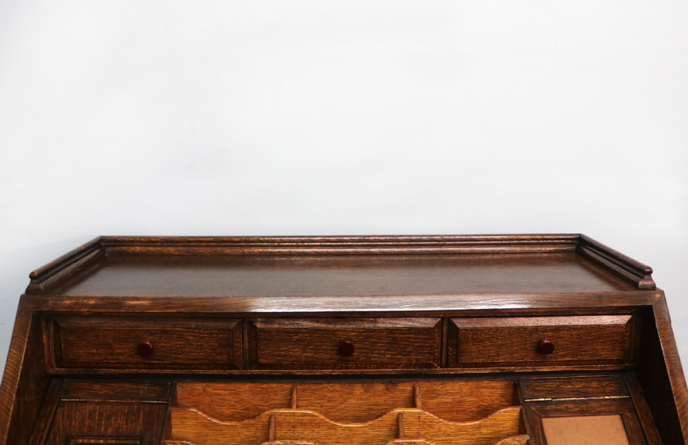 A dark oak fall-front bureau with octagonal geometric cupboard doors, carved details, turned gadrooned feet, and an open fitted stationery compartment. View XIX