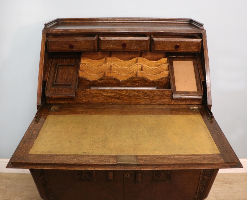 A dark oak fall-front bureau with octagonal geometric cupboard doors, carved details, turned gadrooned feet, and an open fitted stationery compartment. View XX