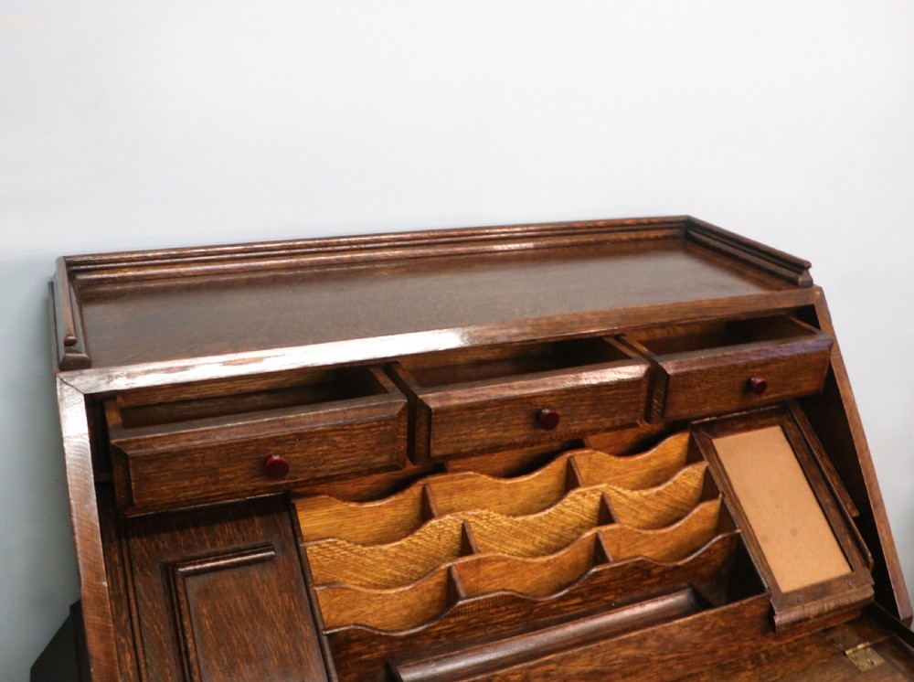 A dark oak fall-front bureau with octagonal geometric cupboard doors, carved details, turned gadrooned feet, and an open fitted stationery compartment. View XXI