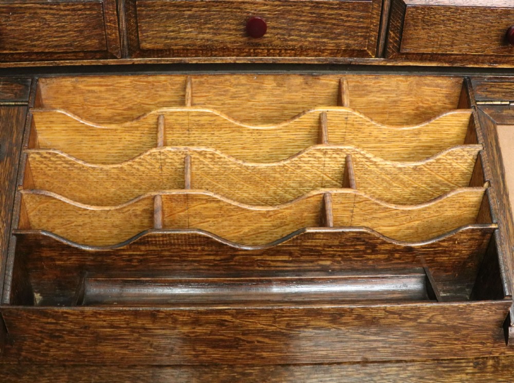 A dark oak fall-front bureau with octagonal geometric cupboard doors, carved details, turned gadrooned feet, and an open fitted stationery compartment. View XXVI