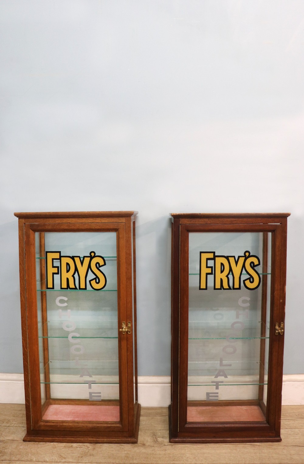 A pair of early 20th-century wooden glazed counter display cabinets featuring sign-written Frys Chocolate lettering on the front glass panels and interior glass shelves.