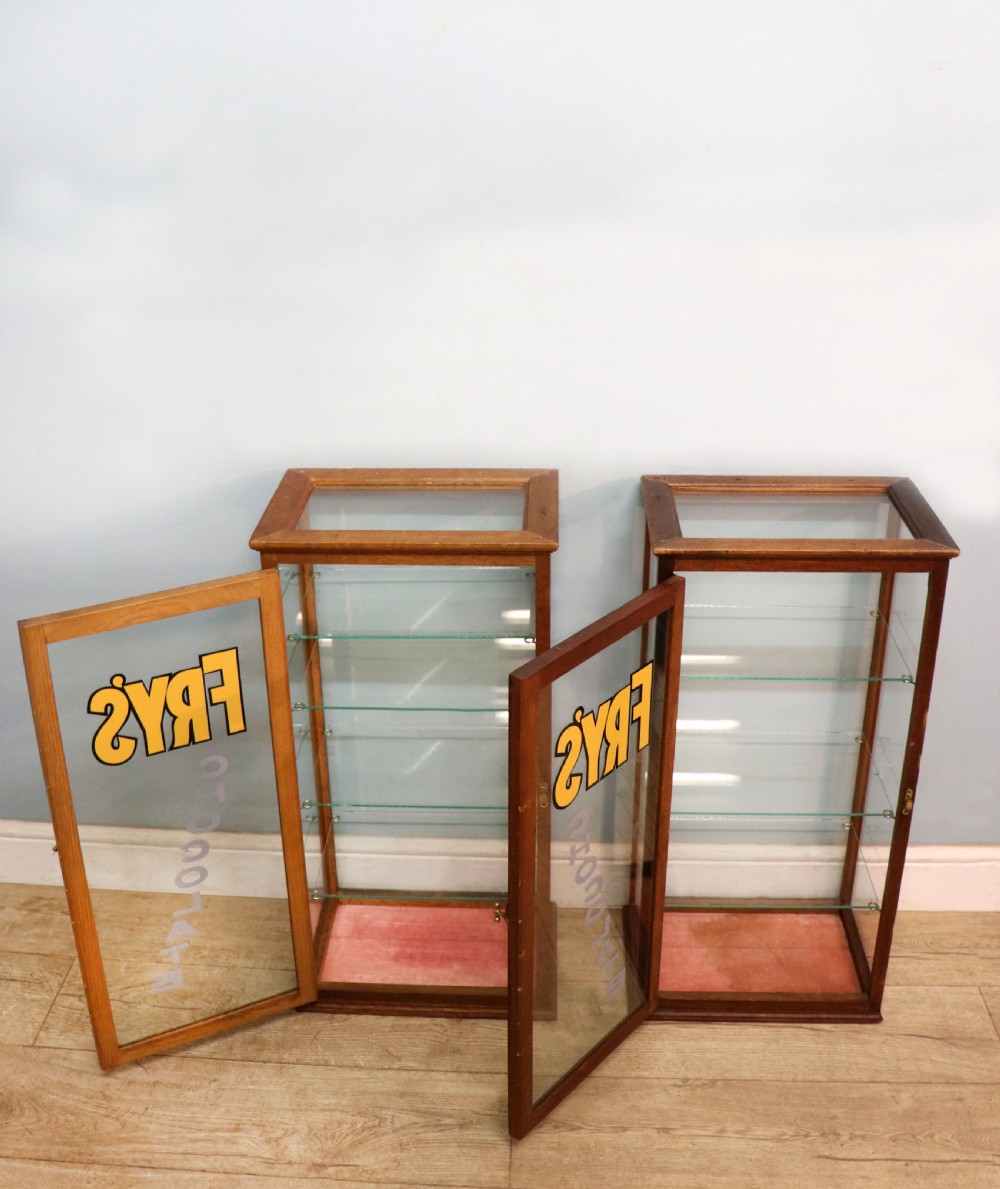 A pair of early 20th-century wooden glazed counter display cabinets featuring sign-written Frys Chocolate lettering on the front glass panels and interior glass shelves. View V