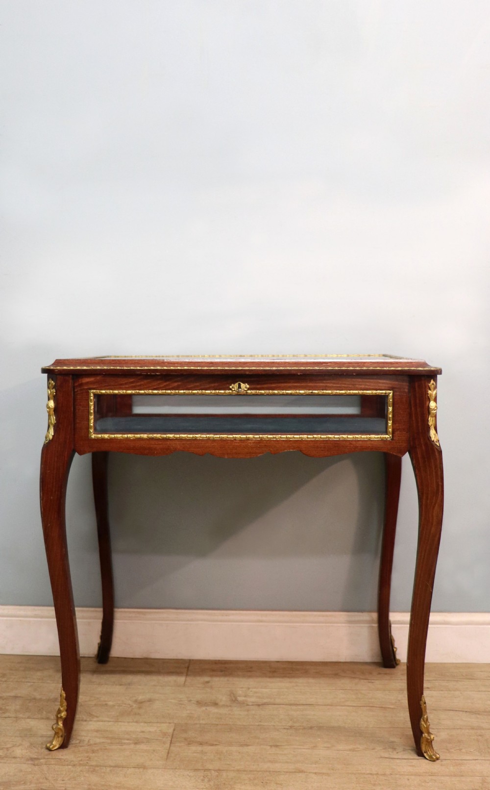 A French Louis XV style glazed bijouterie table in dark hardwood with cabriole legs, gilt metal mounts, and blue Breitling lettering on the glass top. View III