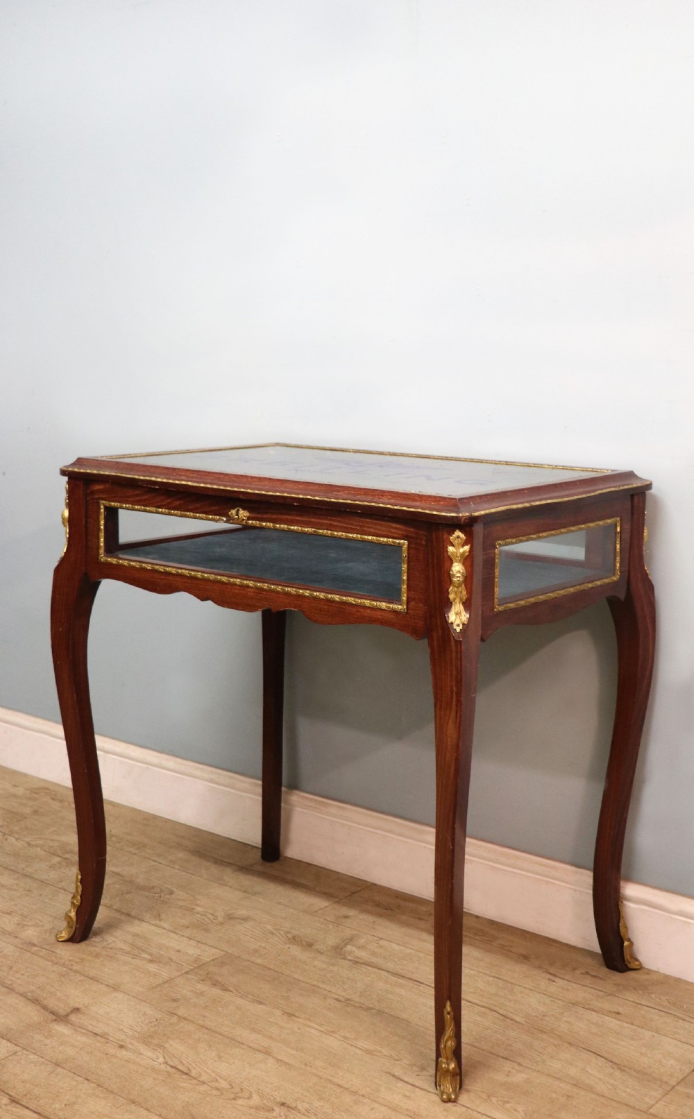 A French Louis XV style glazed bijouterie table in dark hardwood with cabriole legs, gilt metal mounts, and blue Breitling lettering on the glass top. View VI