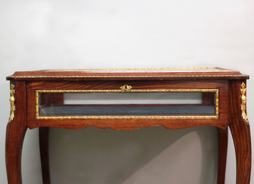 A French Louis XV style glazed bijouterie table in dark hardwood with cabriole legs, gilt metal mounts, and blue Breitling lettering on the glass top. View IX