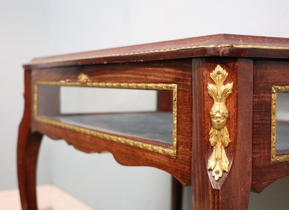 A French Louis XV style glazed bijouterie table in dark hardwood with cabriole legs, gilt metal mounts, and blue Breitling lettering on the glass top. View XV