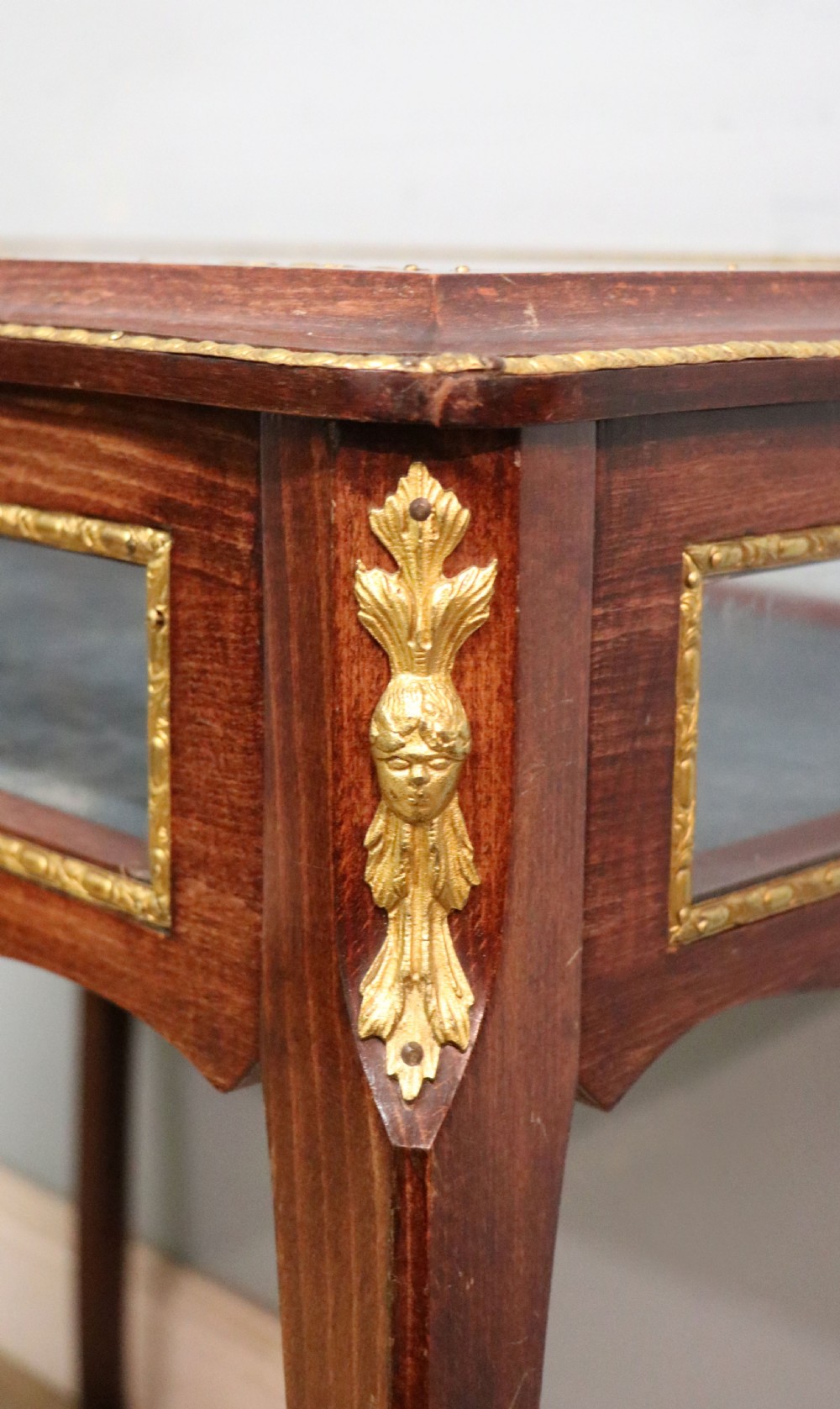 A French Louis XV style glazed bijouterie table in dark hardwood with cabriole legs, gilt metal mounts, and blue Breitling lettering on the glass top. View XVI