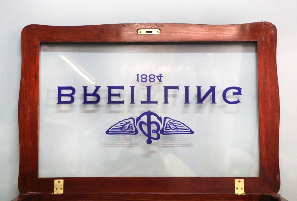 A French Louis XV style glazed bijouterie table in dark hardwood with cabriole legs, gilt metal mounts, and blue Breitling lettering on the glass top. View XVIII