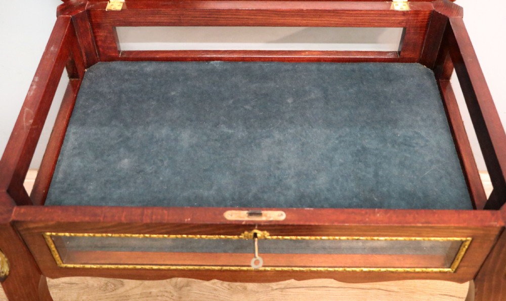 A French Louis XV style glazed bijouterie table in dark hardwood with cabriole legs, gilt metal mounts, and blue Breitling lettering on the glass top. View XXVI