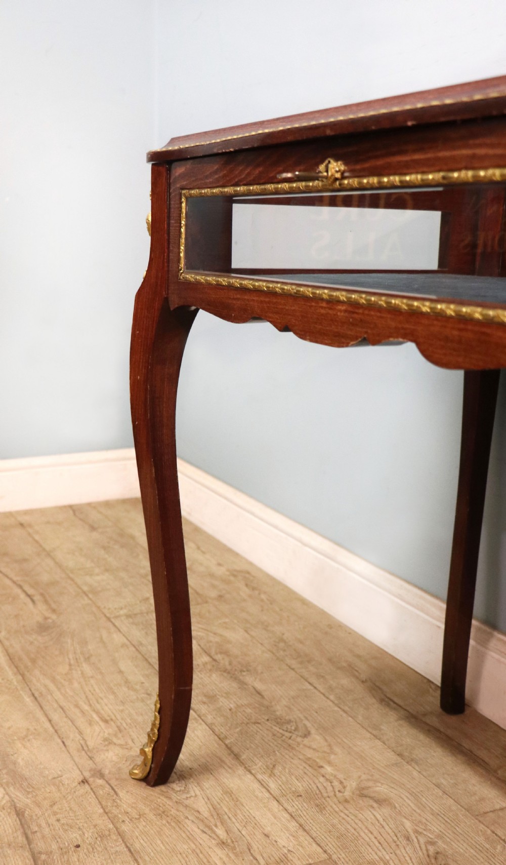 A French Louis XV style glazed bijouterie table in dark hardwood with cabriole legs, gilt metal mounts, and blue Breitling lettering on the glass top. View XXVII