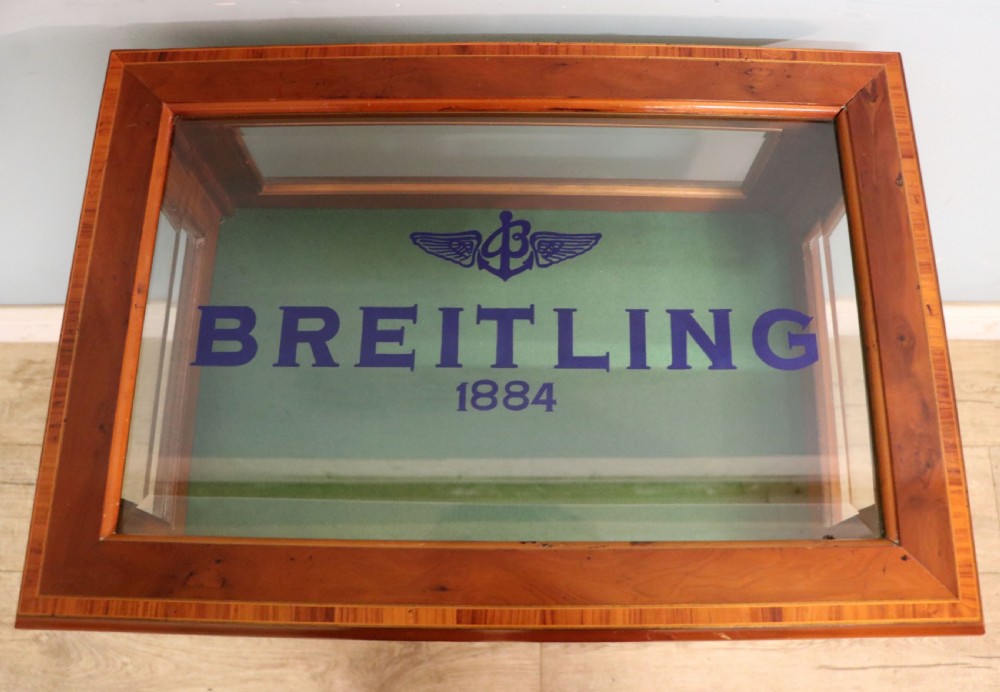A glazed yew wood bijouterie display table featuring a green velvet interior lining, lower undertier, and Breitling 1884 logo printed on the top glass. View II