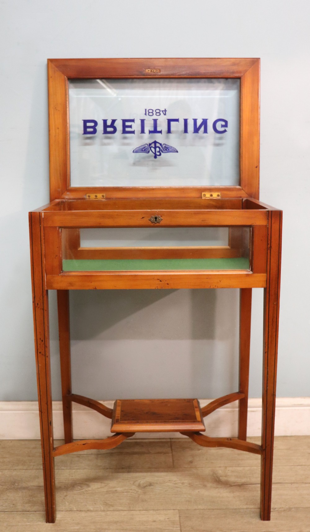A glazed yew wood bijouterie display table featuring a green velvet interior lining, lower undertier, and Breitling 1884 logo printed on the top glass. View III