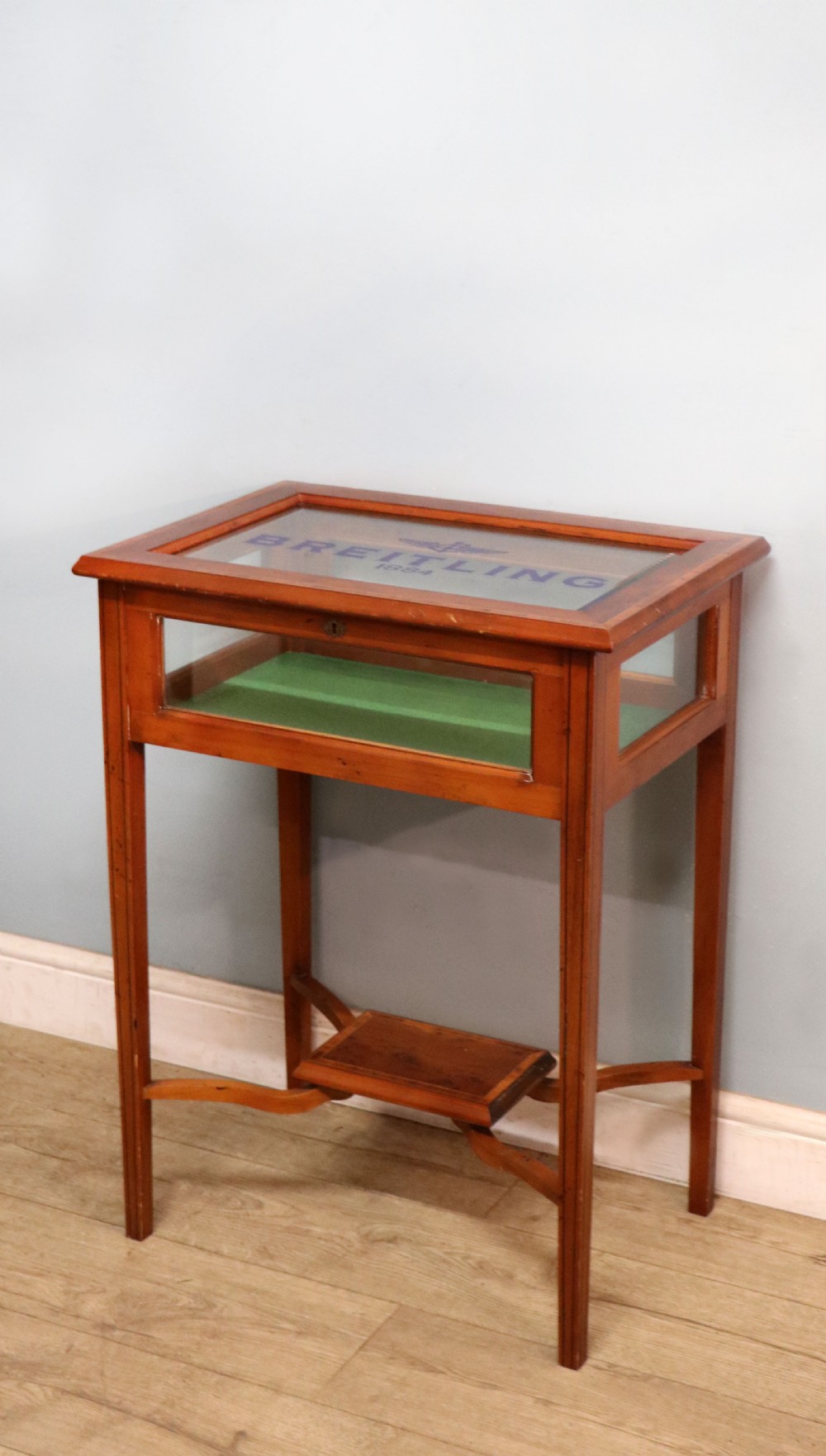 A glazed yew wood bijouterie display table featuring a green velvet interior lining, lower undertier, and Breitling 1884 logo printed on the top glass. View V