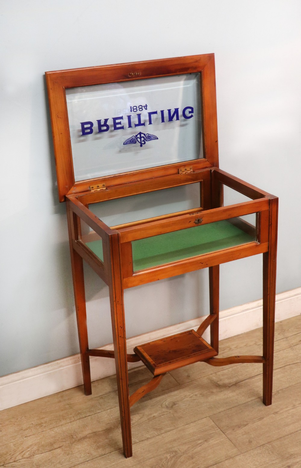 A glazed yew wood bijouterie display table featuring a green velvet interior lining, lower undertier, and Breitling 1884 logo printed on the top glass. View VI