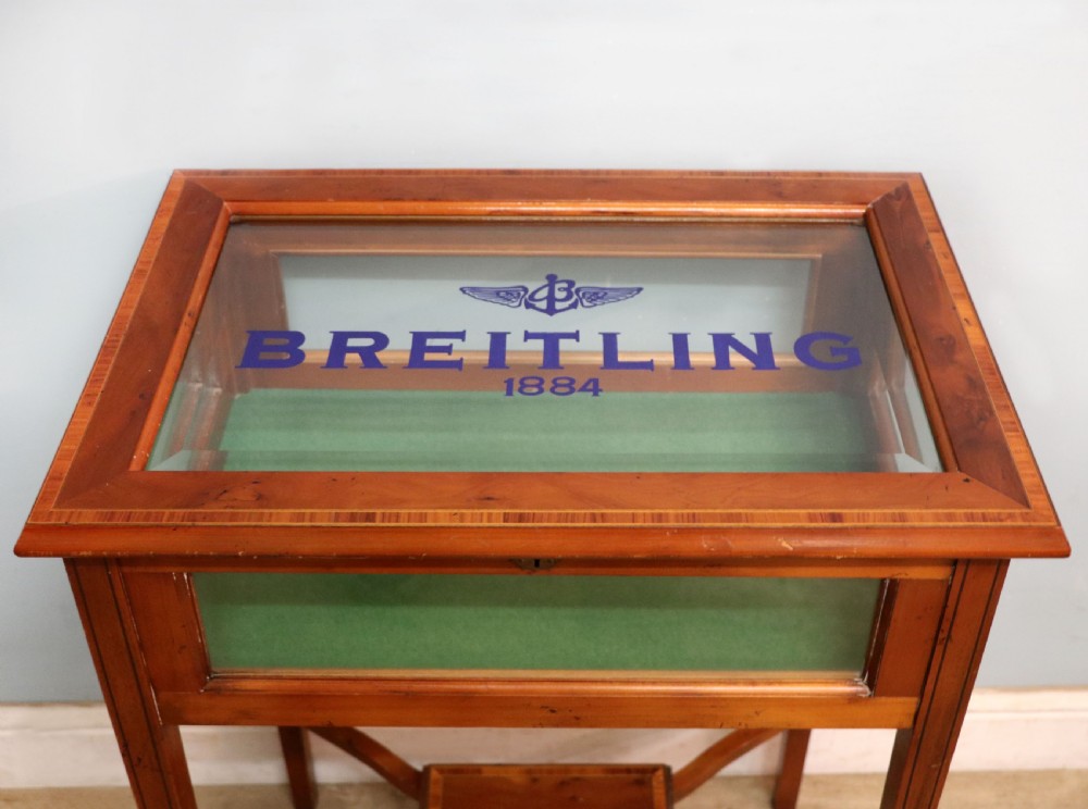 A glazed yew wood bijouterie display table featuring a green velvet interior lining, lower undertier, and Breitling 1884 logo printed on the top glass. View VII