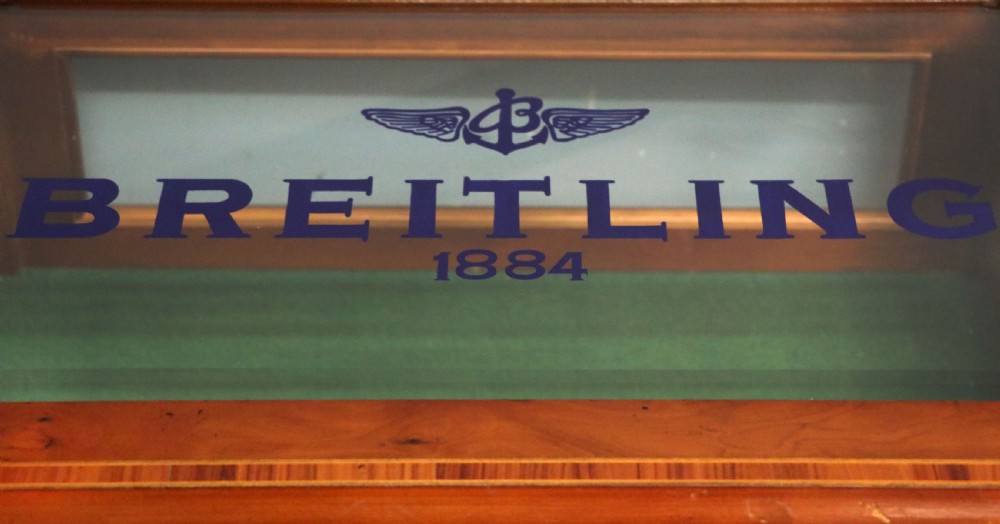 A glazed yew wood bijouterie display table featuring a green velvet interior lining, lower undertier, and Breitling 1884 logo printed on the top glass. View VIII