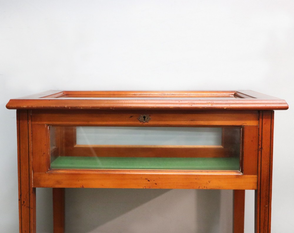 A glazed yew wood bijouterie display table featuring a green velvet interior lining, lower undertier, and Breitling 1884 logo printed on the top glass. View XI