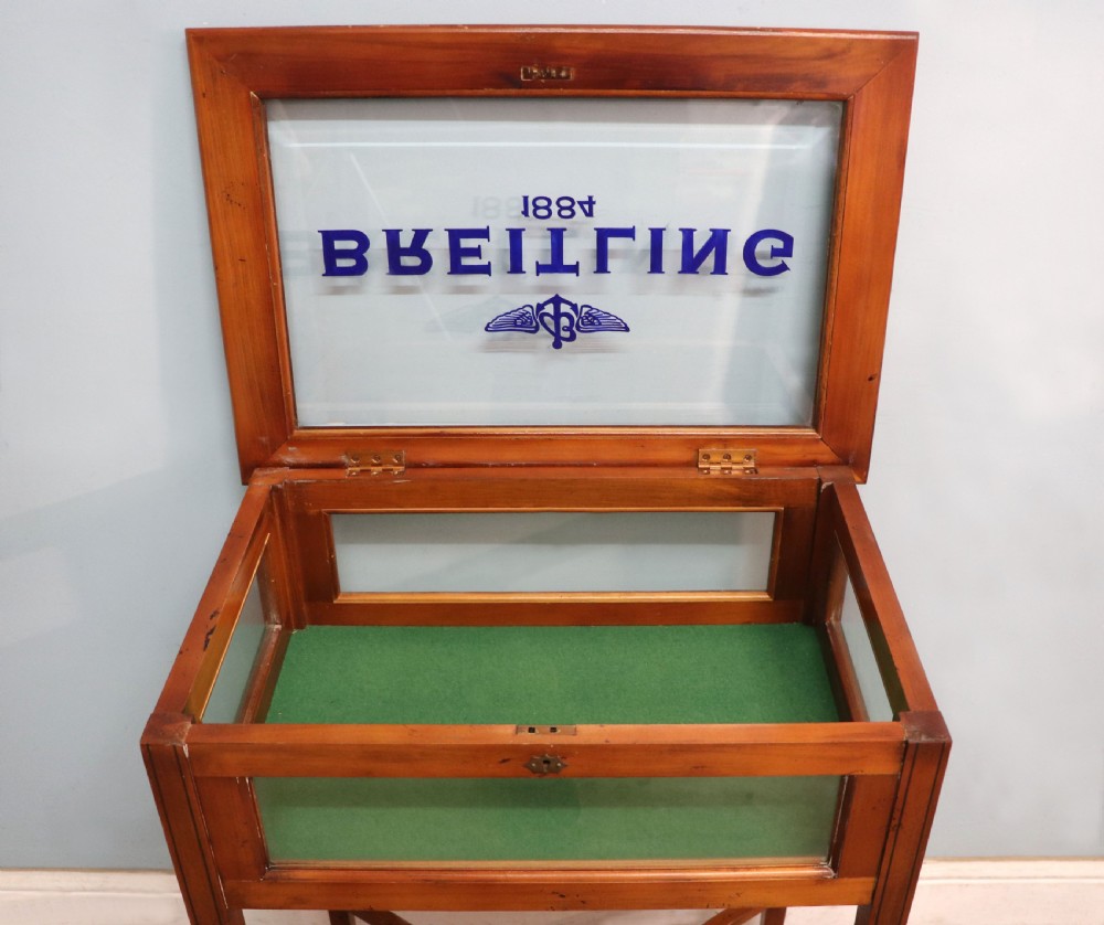 A glazed yew wood bijouterie display table featuring a green velvet interior lining, lower undertier, and Breitling 1884 logo printed on the top glass. View XIV