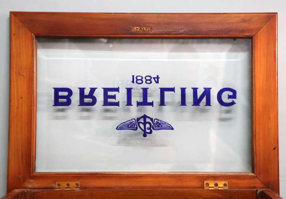 A glazed yew wood bijouterie display table featuring a green velvet interior lining, lower undertier, and Breitling 1884 logo printed on the top glass. View XV