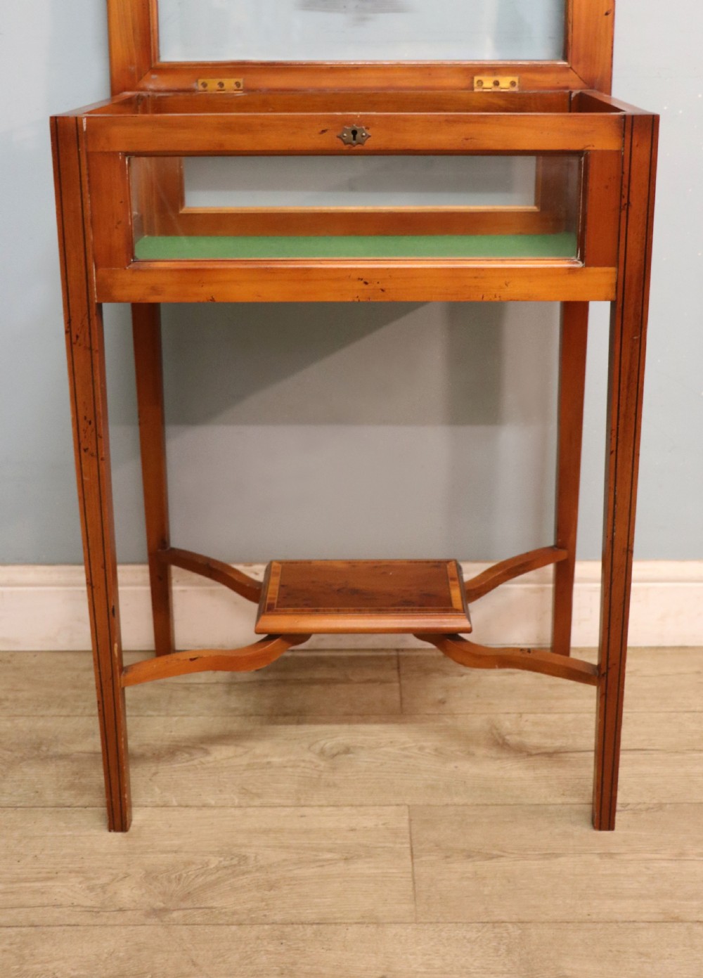 A glazed yew wood bijouterie display table featuring a green velvet interior lining, lower undertier, and Breitling 1884 logo printed on the top glass. View XVIII
