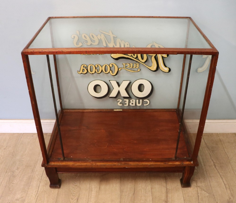 A glazed hardwood countertop display cabinet with sign-written lettering for Rowntrees Elect Cocoa and OXO Cubes on the front glass panel. View V