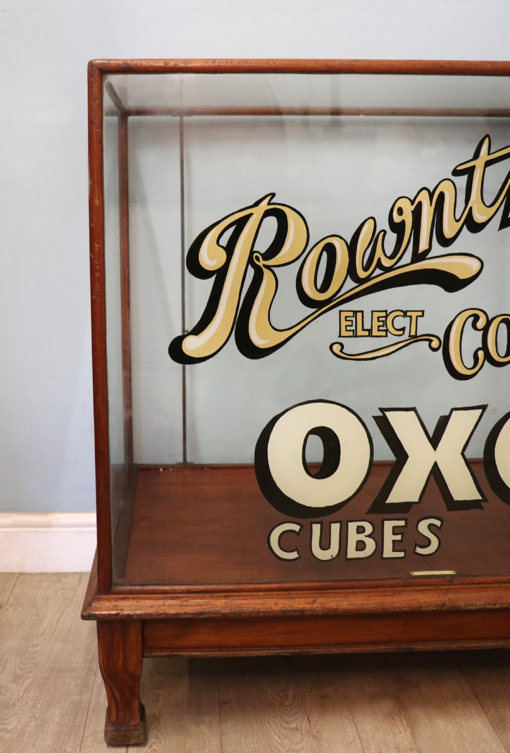 A glazed hardwood countertop display cabinet with sign-written lettering for Rowntrees Elect Cocoa and OXO Cubes on the front glass panel. View VIII