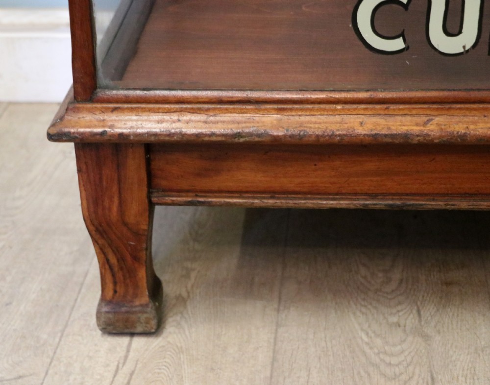 A glazed hardwood countertop display cabinet with sign-written lettering for Rowntrees Elect Cocoa and OXO Cubes on the front glass panel. View XXI