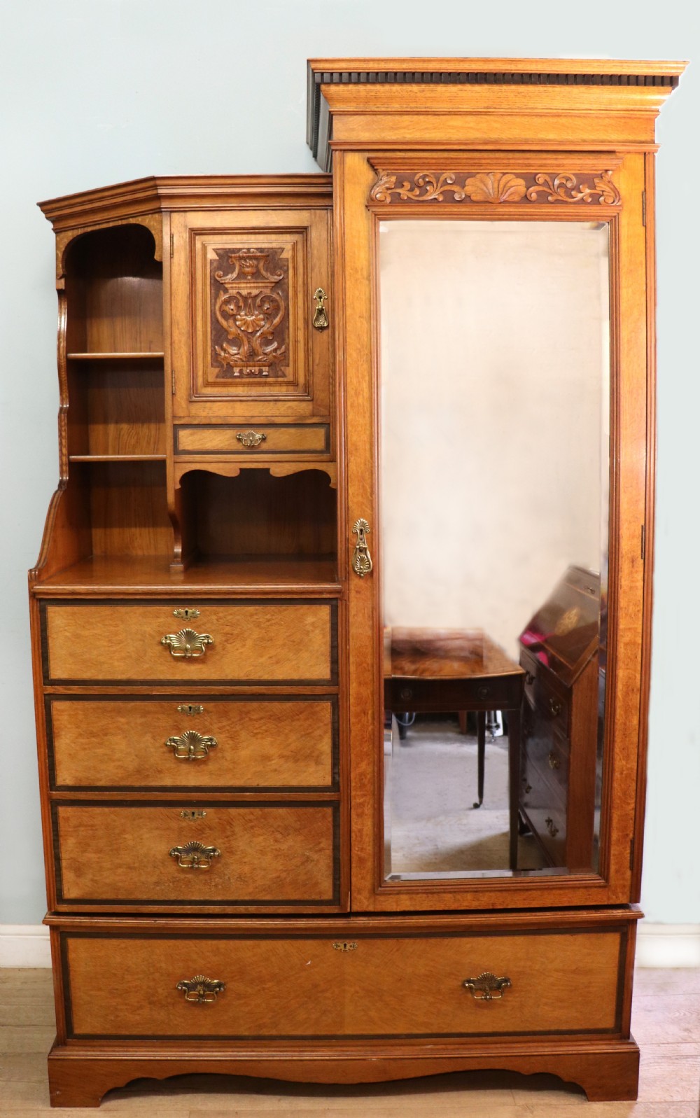 A late nineteenth-century American walnut compendium wardrobe featuring a full-length mirrored door, carved timber motif panel, open side shelving, brass handles, and integrated drawers.