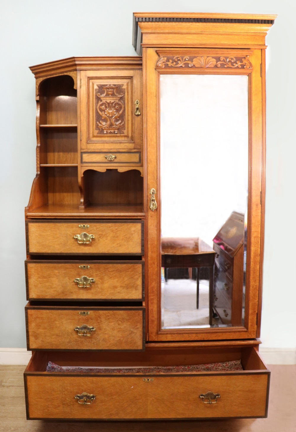 A late nineteenth-century American walnut compendium wardrobe featuring a full-length mirrored door, carved timber motif panel, open side shelving, brass handles, and integrated drawers. View II