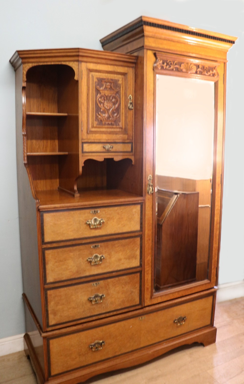 A late nineteenth-century American walnut compendium wardrobe featuring a full-length mirrored door, carved timber motif panel, open side shelving, brass handles, and integrated drawers. View III