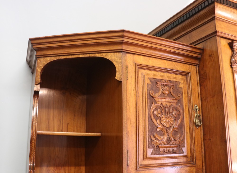 A late nineteenth-century American walnut compendium wardrobe featuring a full-length mirrored door, carved timber motif panel, open side shelving, brass handles, and integrated drawers. View V