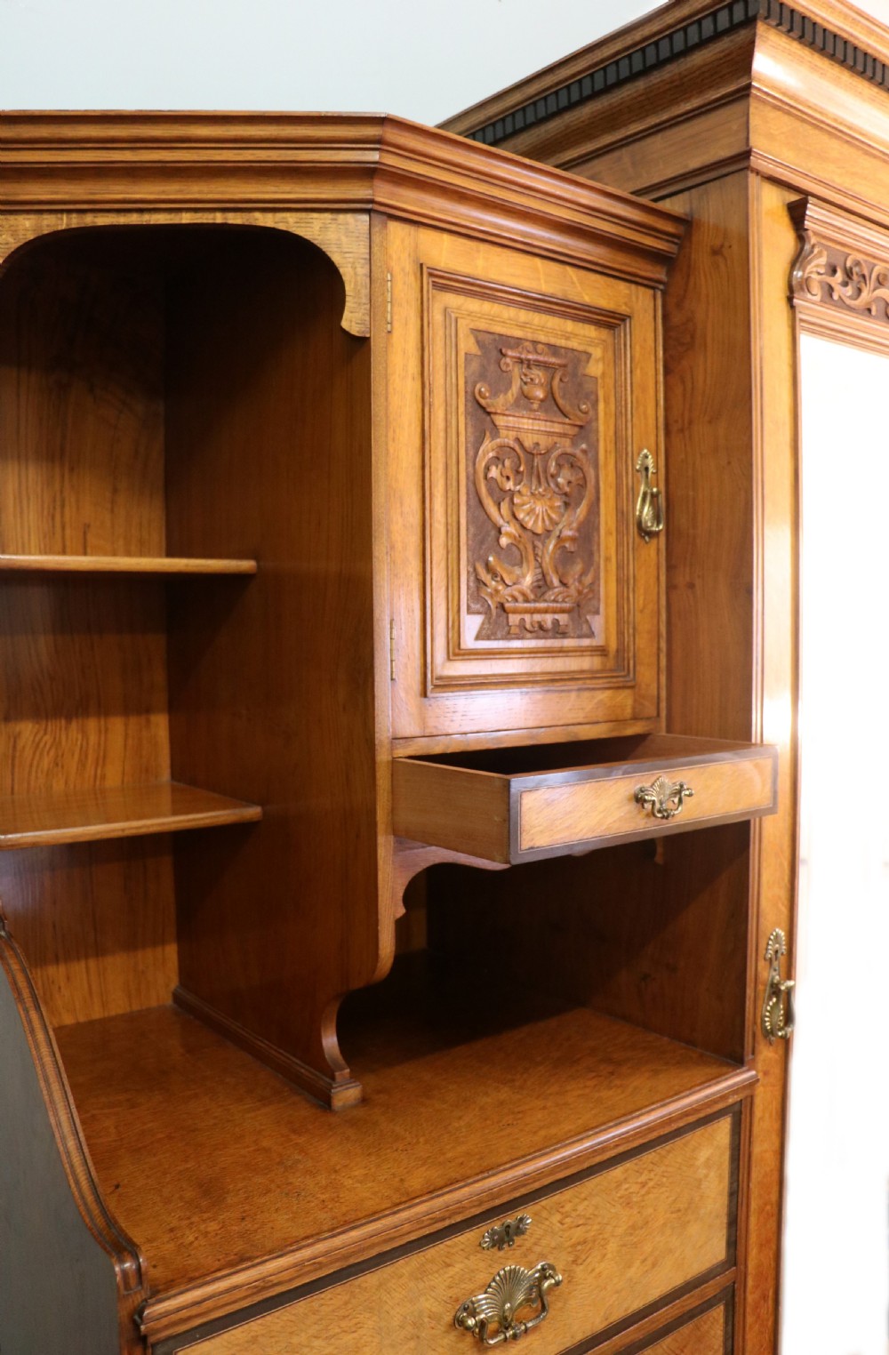 A late nineteenth-century American walnut compendium wardrobe featuring a full-length mirrored door, carved timber motif panel, open side shelving, brass handles, and integrated drawers. View VI