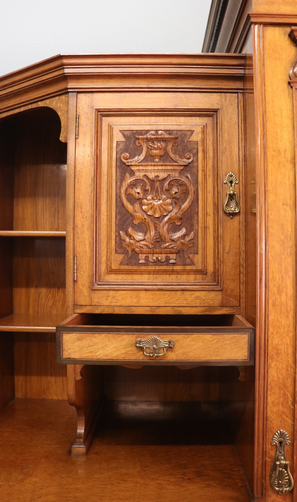 A late nineteenth-century American walnut compendium wardrobe featuring a full-length mirrored door, carved timber motif panel, open side shelving, brass handles, and integrated drawers. View VII