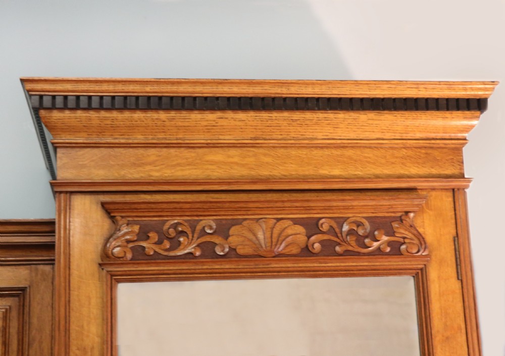 A late nineteenth-century American walnut compendium wardrobe featuring a full-length mirrored door, carved timber motif panel, open side shelving, brass handles, and integrated drawers. View XXIV
