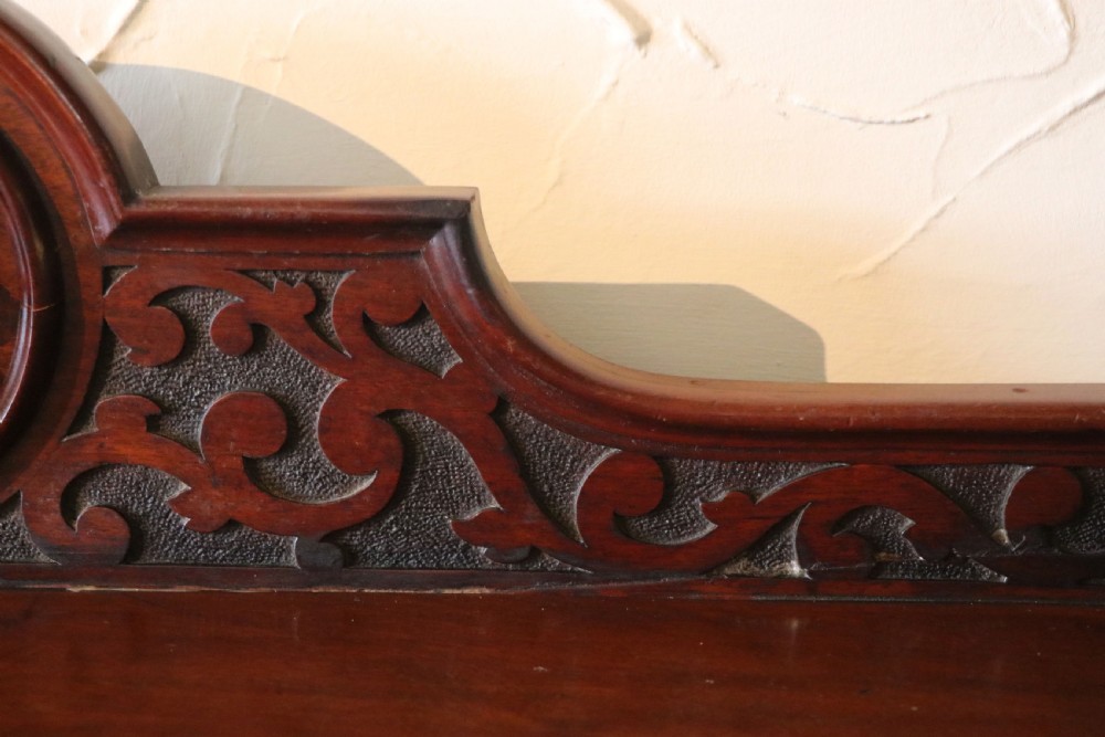 A Victorian mahogany three-tiered dumb waiter featuring carved decorative pediments, supporting brackets, lower drawers, and ceramic castors. View XIII