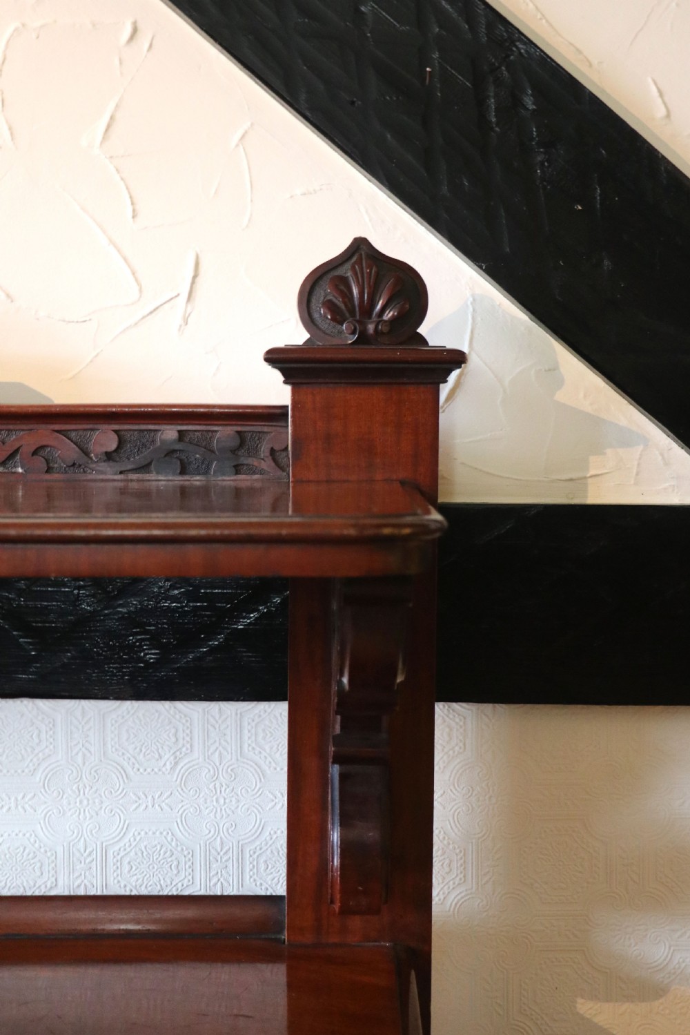 A Victorian mahogany three-tiered dumb waiter featuring carved decorative pediments, supporting brackets, lower drawers, and ceramic castors. View XIV
