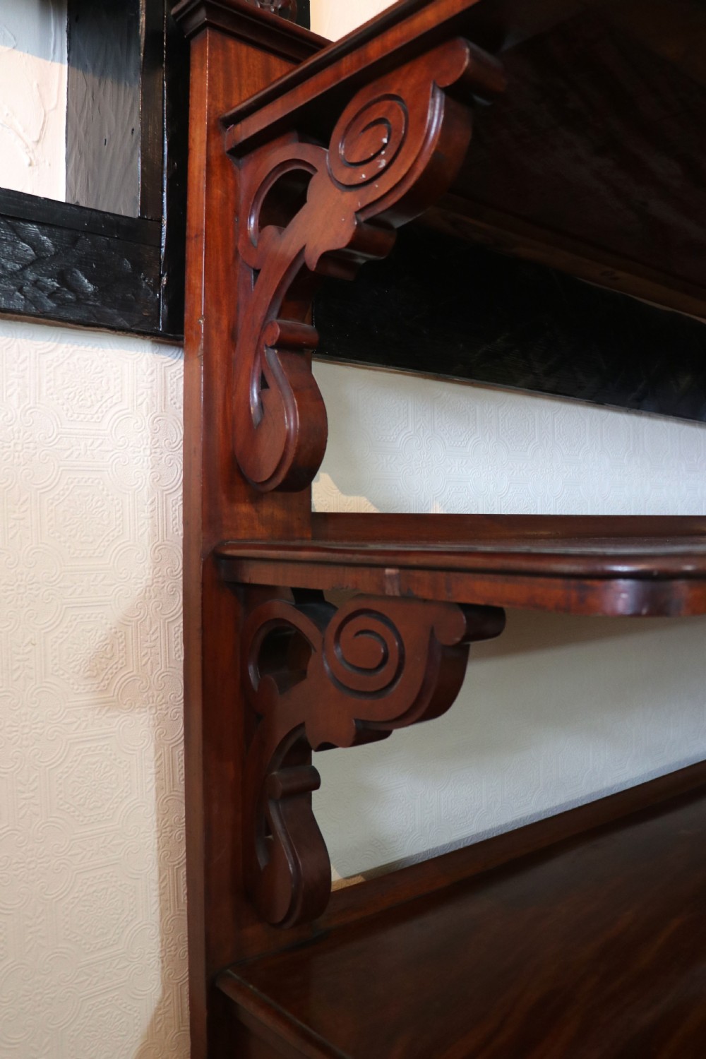 A Victorian mahogany three-tiered dumb waiter featuring carved decorative pediments, supporting brackets, lower drawers, and ceramic castors. View XVIII