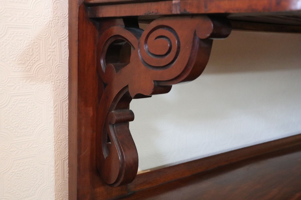 A Victorian mahogany three-tiered dumb waiter featuring carved decorative pediments, supporting brackets, lower drawers, and ceramic castors. View XIX