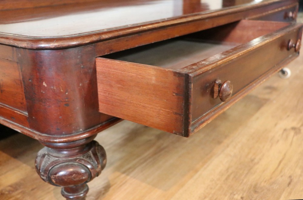 A Victorian mahogany three-tiered dumb waiter featuring carved decorative pediments, supporting brackets, lower drawers, and ceramic castors. View XXII