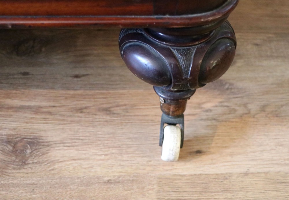 A Victorian mahogany three-tiered dumb waiter featuring carved decorative pediments, supporting brackets, lower drawers, and ceramic castors. View XXIII