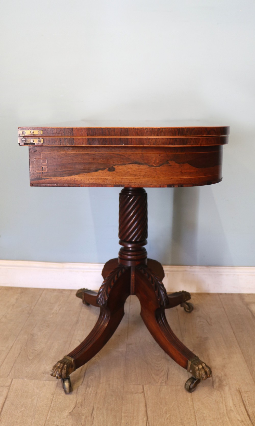 A late Georgian dark rosewood card table featuring an open fold-over green baize top supported on a spiral-carved pedestal and splayed legs with brass paw castors. View II