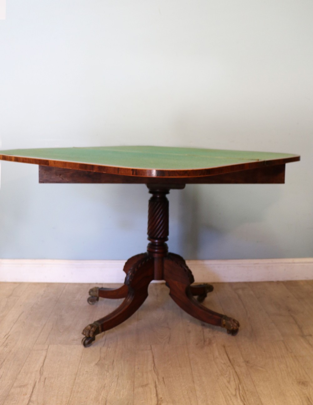 A late Georgian dark rosewood card table featuring an open fold-over green baize top supported on a spiral-carved pedestal and splayed legs with brass paw castors. View III