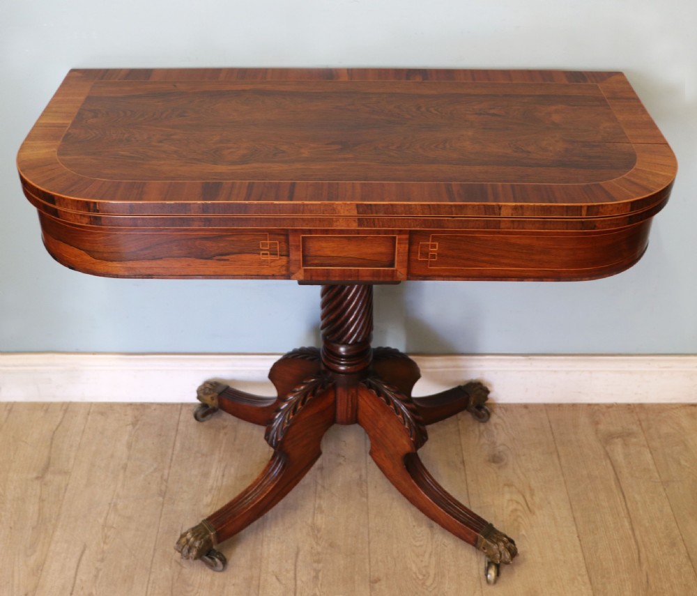 A late Georgian dark rosewood card table featuring an open fold-over green baize top supported on a spiral-carved pedestal and splayed legs with brass paw castors. View IV