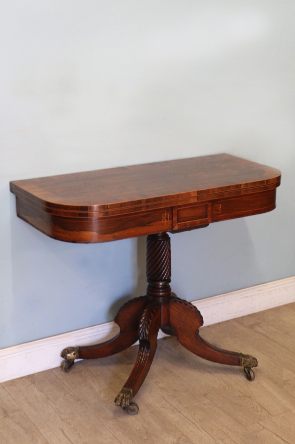 A late Georgian dark rosewood card table featuring an open fold-over green baize top supported on a spiral-carved pedestal and splayed legs with brass paw castors. View V