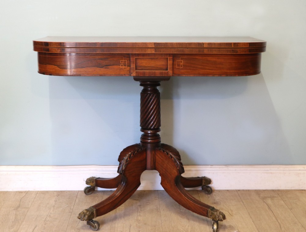 A late Georgian dark rosewood card table featuring an open fold-over green baize top supported on a spiral-carved pedestal and splayed legs with brass paw castors. View VI