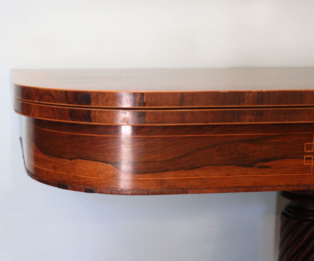 A late Georgian dark rosewood card table featuring an open fold-over green baize top supported on a spiral-carved pedestal and splayed legs with brass paw castors. View VII