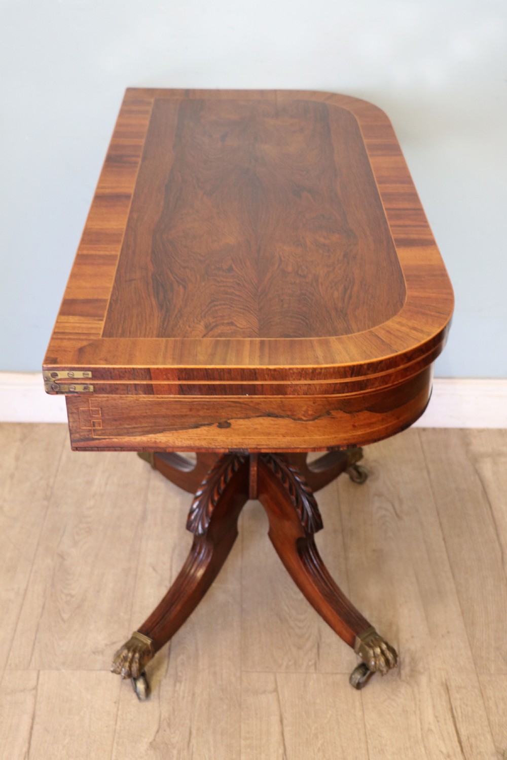 A late Georgian dark rosewood card table featuring an open fold-over green baize top supported on a spiral-carved pedestal and splayed legs with brass paw castors. View IX