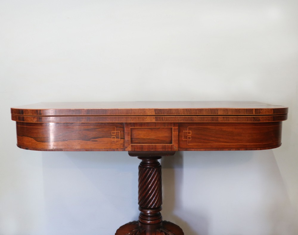 A late Georgian dark rosewood card table featuring an open fold-over green baize top supported on a spiral-carved pedestal and splayed legs with brass paw castors. View XI