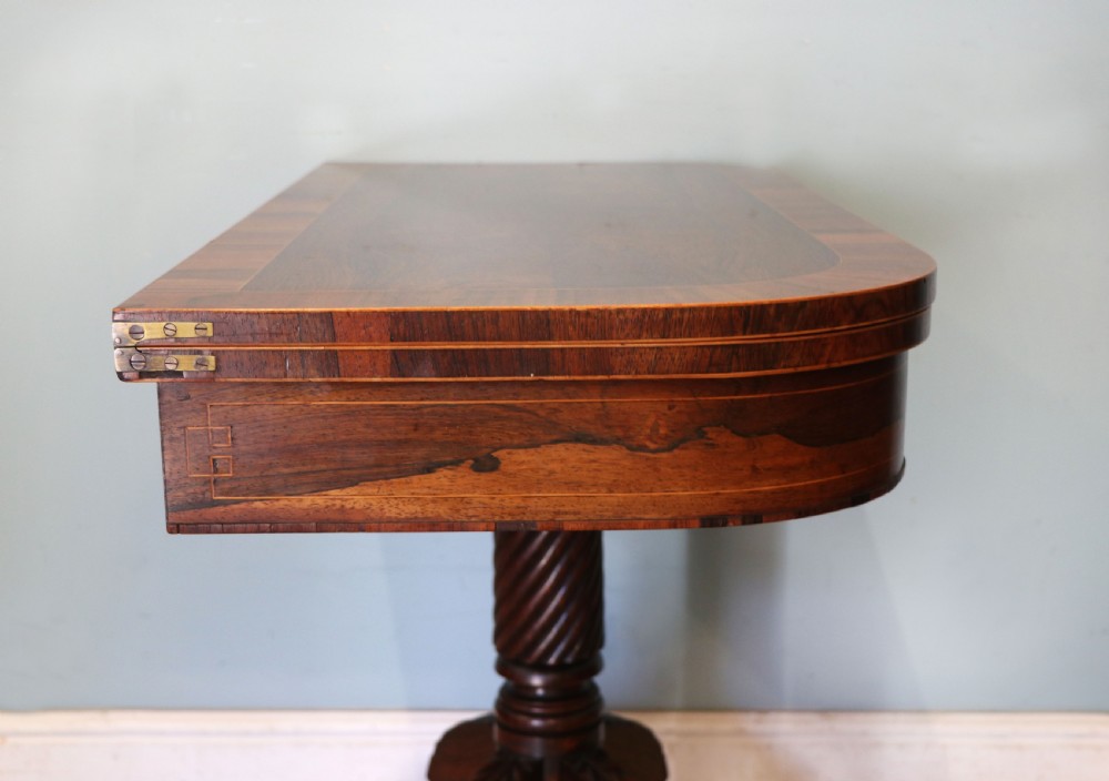 A late Georgian dark rosewood card table featuring an open fold-over green baize top supported on a spiral-carved pedestal and splayed legs with brass paw castors. View XVI