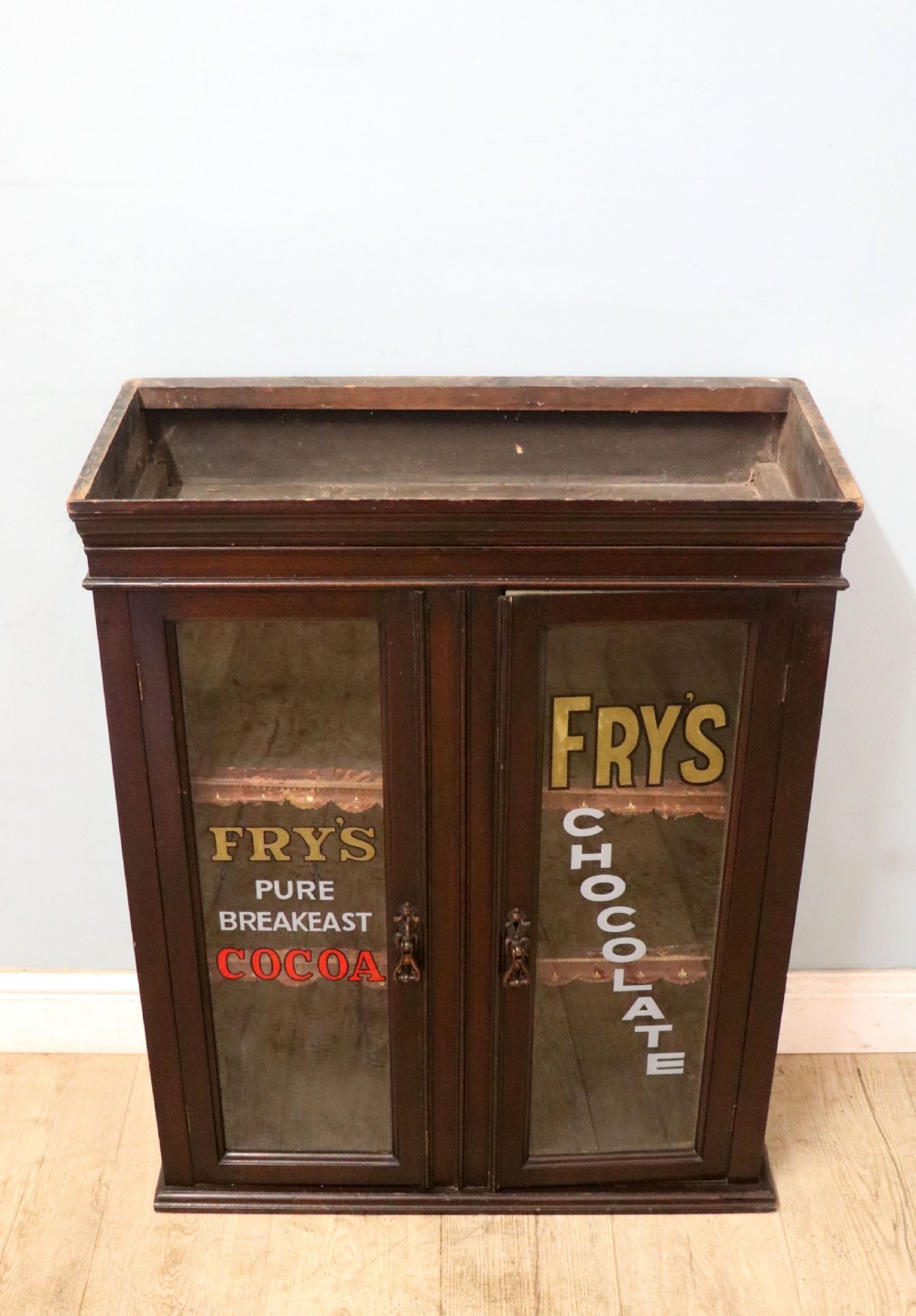 A dark mahogany Victorian display cabinet featuring glazed doors painted with Frys Cocoa and Chocolate advertising typography.